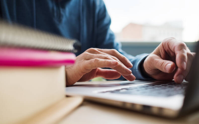 Person typing on a laptop on a table with books